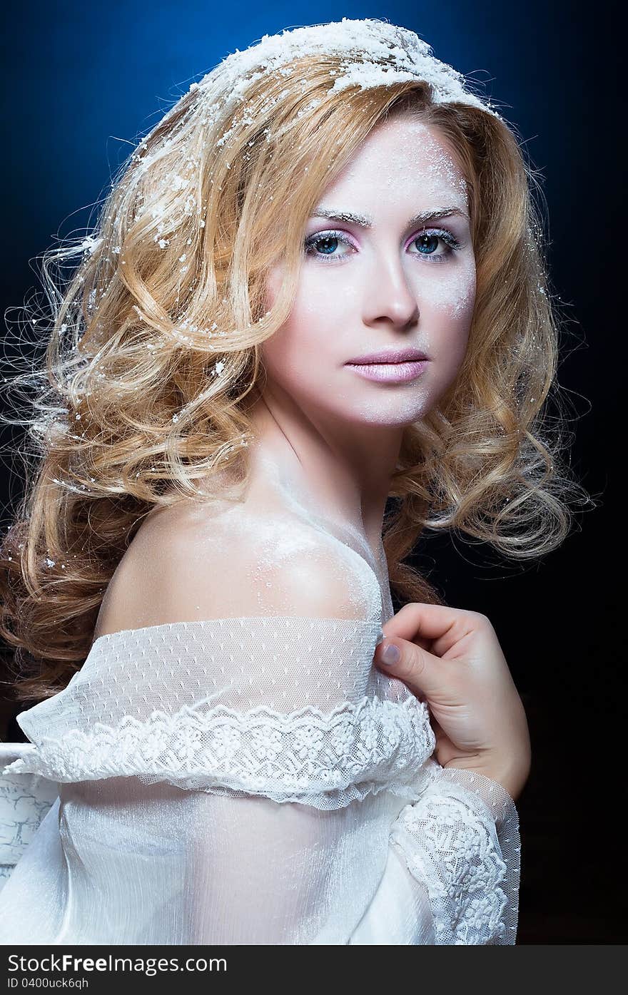 The beautiful blond girl with a winter make-up in a white attire on a dark blue background