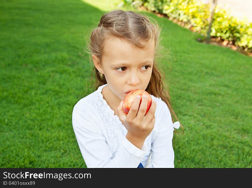 A pretty girl with long hair, eating red apple sitting on green grass. A pretty girl with long hair, eating red apple sitting on green grass