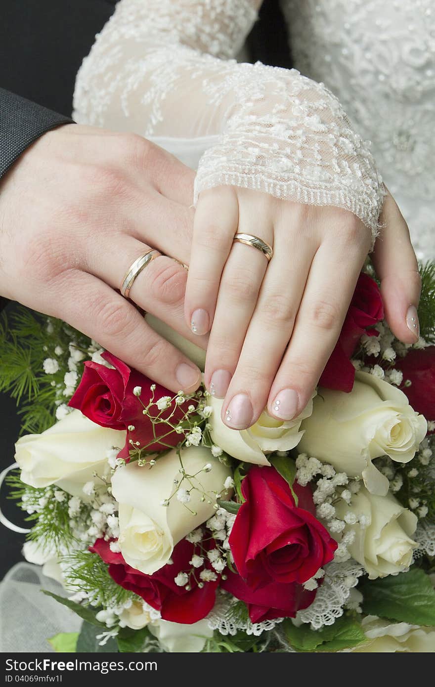 Hands of the newlyweds with wedding rings on a bouquet of roses. Hands of the newlyweds with wedding rings on a bouquet of roses