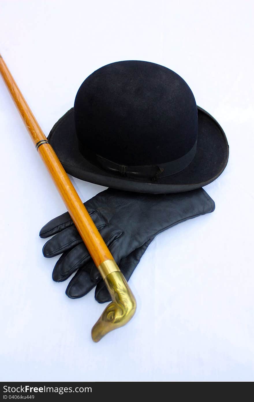 A vintage black derby with black leather gloves and a wooden cane with a duck head sitting on a white cloth covered table. A vintage black derby with black leather gloves and a wooden cane with a duck head sitting on a white cloth covered table