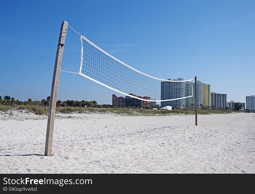 A beach volleyball net with buildings in the background, on a sunny day.