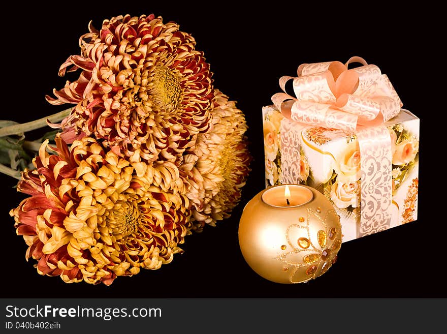 A beautiful bouquet of chrysanthemums, a gift and lighted candle on a black background. A beautiful bouquet of chrysanthemums, a gift and lighted candle on a black background