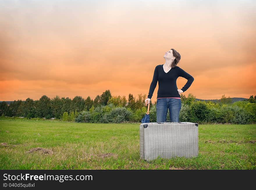 Young woman standing on a meadow with suitcase and umbrella. Young woman standing on a meadow with suitcase and umbrella