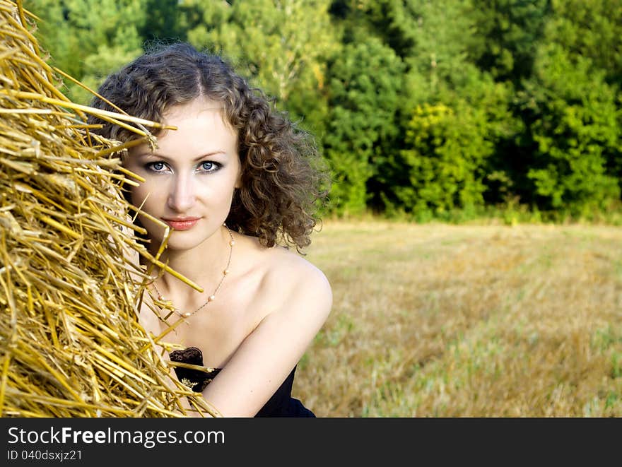 Beautiful curly girl near the sheaf of hay in nature. Beautiful curly girl near the sheaf of hay in nature