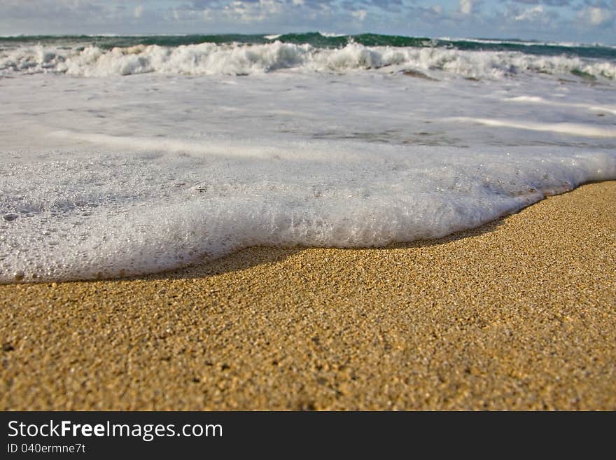 Ground perspective of an incoming tide with foam and golden sand. Ground perspective of an incoming tide with foam and golden sand