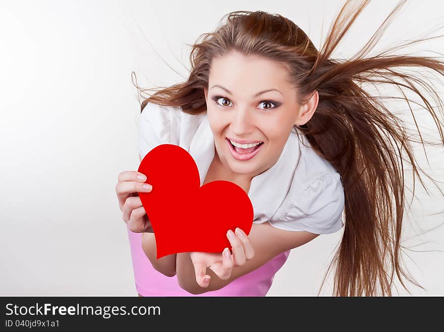 Smiling young woman holding a heart, on a light background