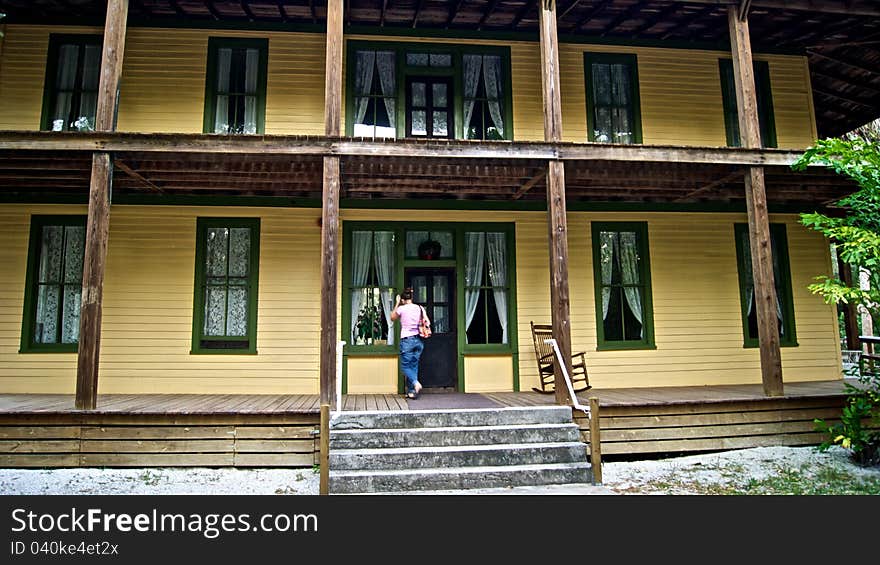 A young woman stands on the porch of an old wooden house built in early 1900's in historic area of estero florida. There is an old wooden rocking chair on porch. Koreshan state Park. A young woman stands on the porch of an old wooden house built in early 1900's in historic area of estero florida. There is an old wooden rocking chair on porch. Koreshan state Park.