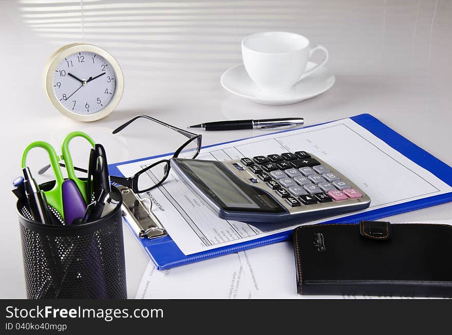 There are calculator, notebook, pen, glasses, cup and clock. There are calculator, notebook, pen, glasses, cup and clock