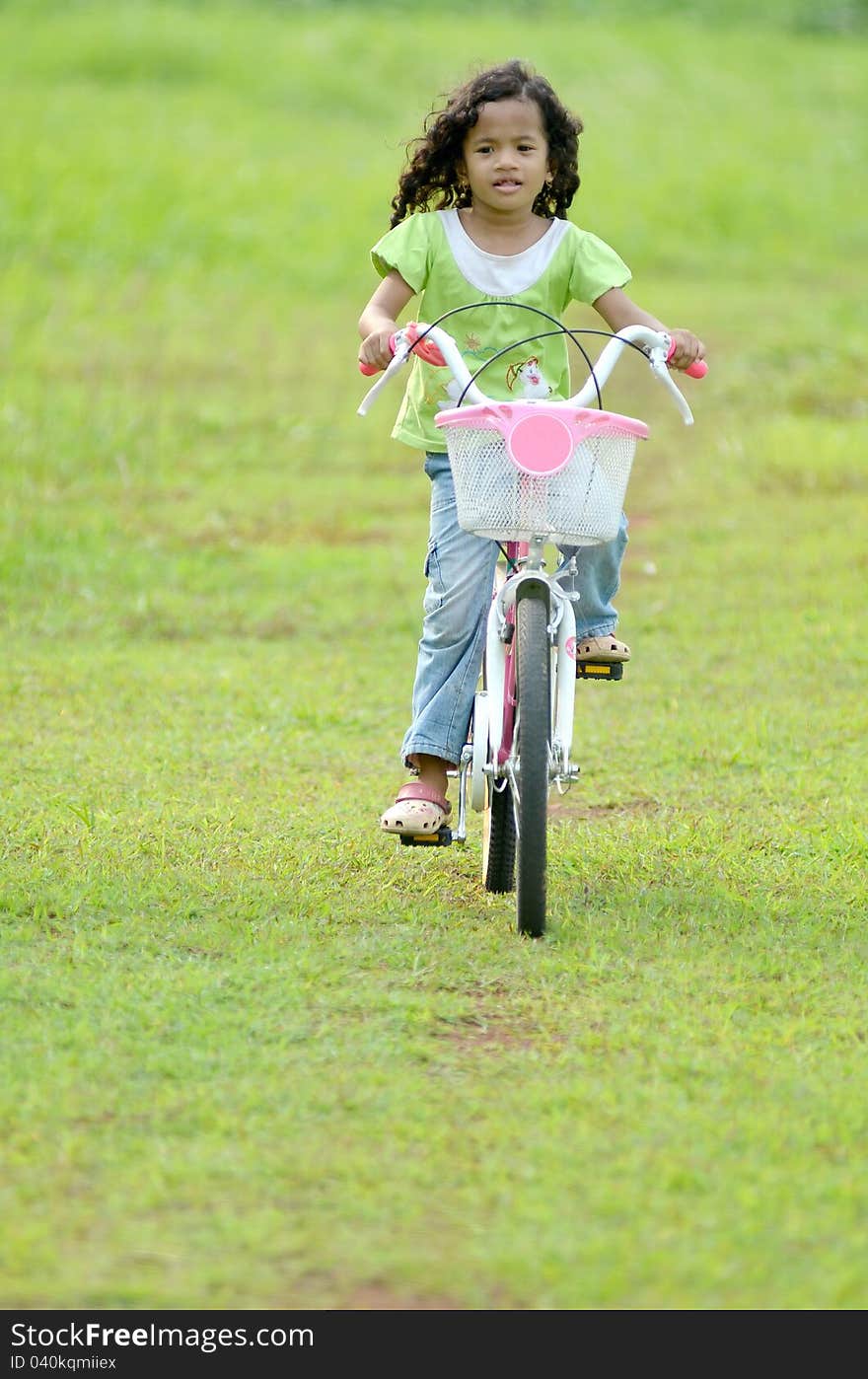 A pretty souteast asian girl with curly hair playing with bike on green grassland. A pretty souteast asian girl with curly hair playing with bike on green grassland.