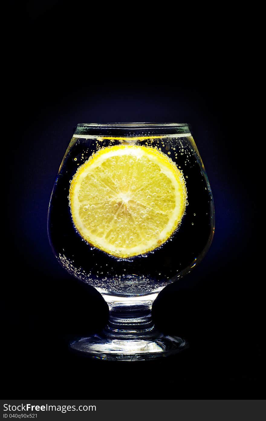 A glass with clear water and lemon isolated on a black background. A glass with clear water and lemon isolated on a black background.