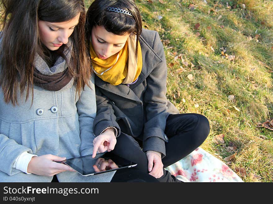 Two teen girls with tablet pc outdoor on the grass