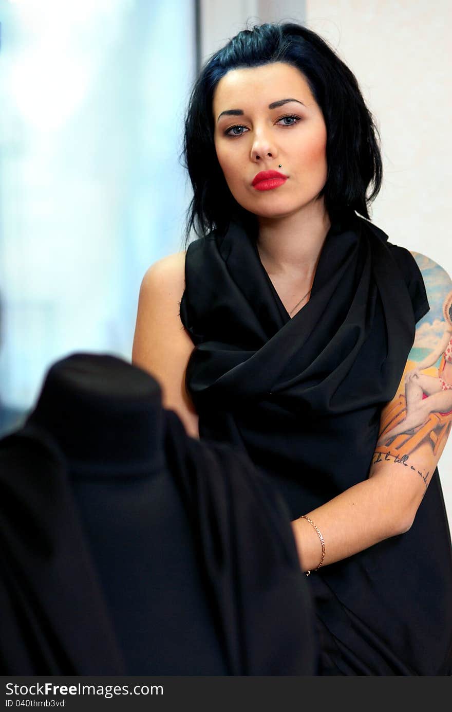 Mannequin wrapped with black cloth with girl with tattoo behind it in seamstress's workshop