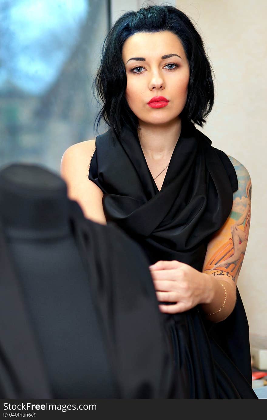 Mannequin wrapped with black cloth with girl with tattoo behind it in seamstress's workshop