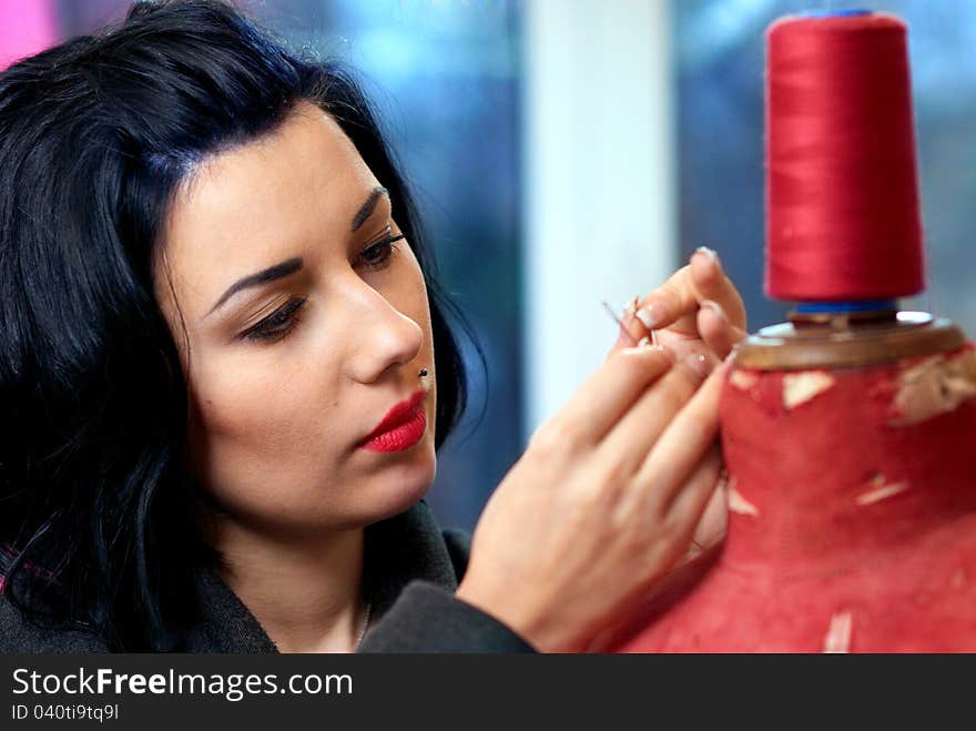 Threading a needle seamstress near red old mannequin in her workshop. Threading a needle seamstress near red old mannequin in her workshop