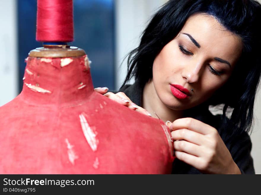 Seamstress repairs red old mannequin with her hands in her workshop in the evening