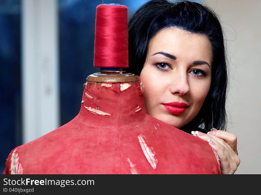 Seamstress repairs red old mannequin with her hands in her workshop in the evening