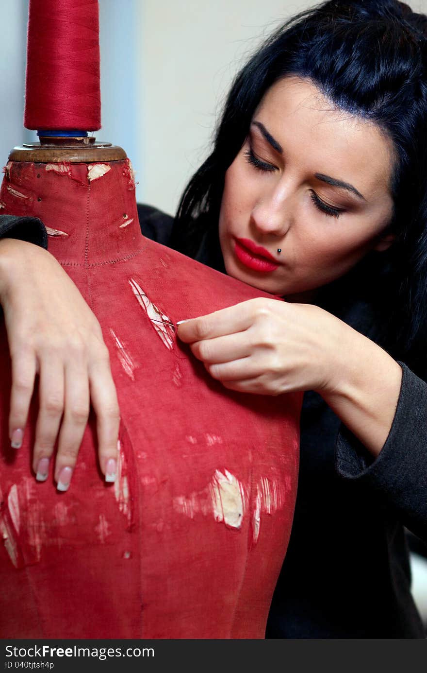 Seamstress repairs red old mannequin with her hands in her workshop in the evening