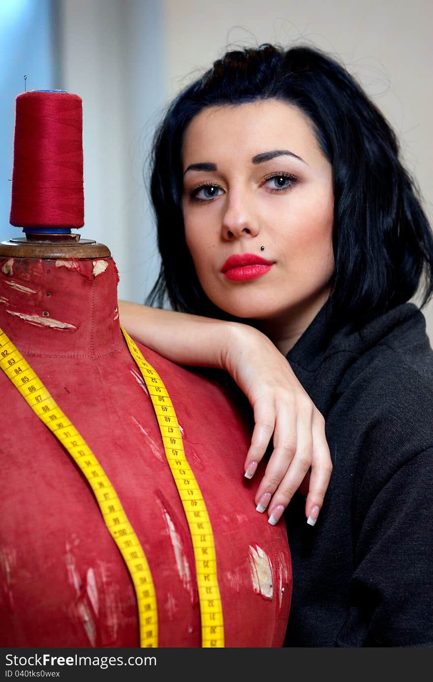 Seamstress with red old mannequin and measuring tape in her workshop