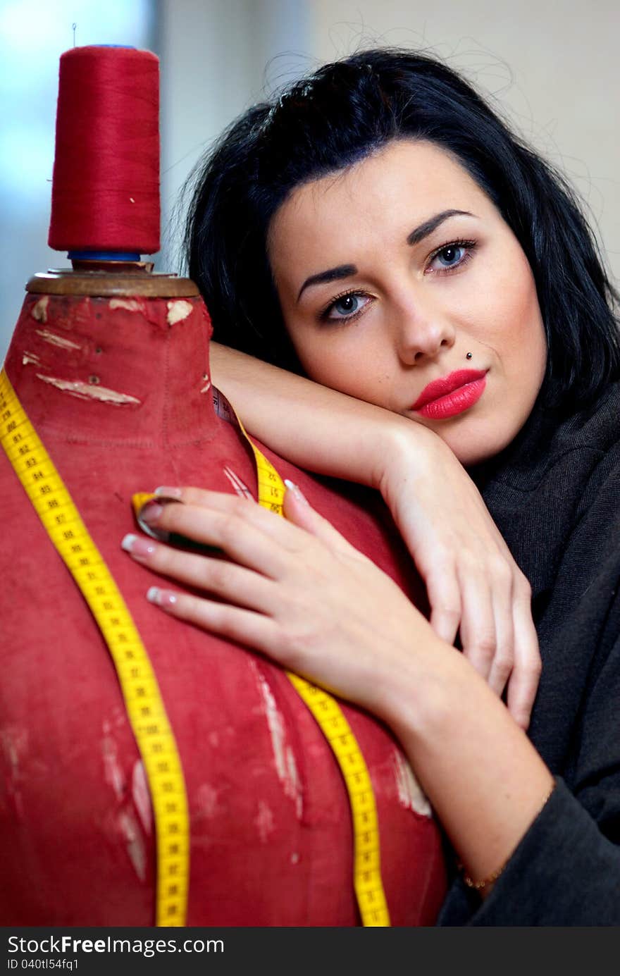 Seamstress with red old mannequin and measuring tape in her workshop