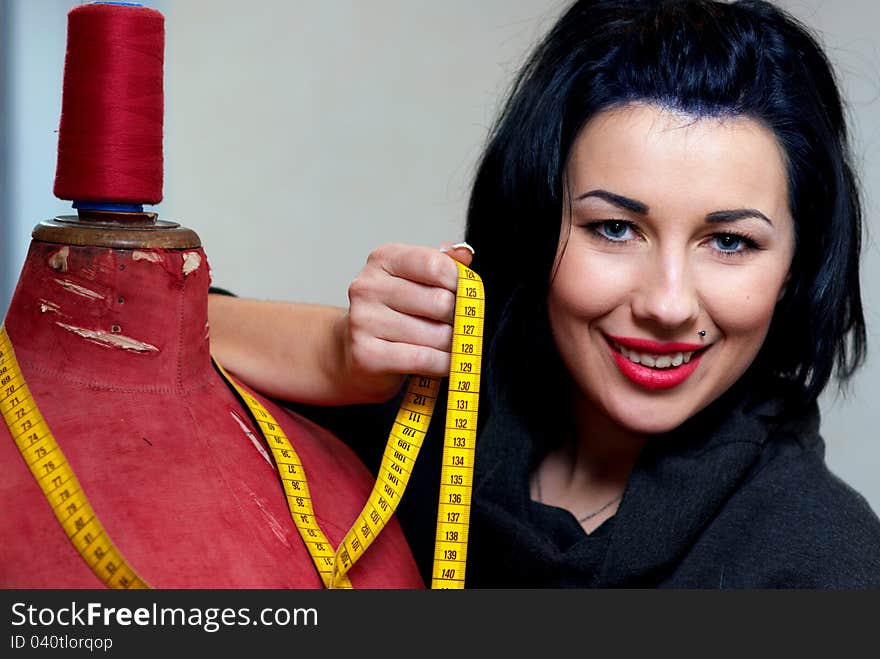 Seamstress with red old mannequin and measuring tape in her workshop