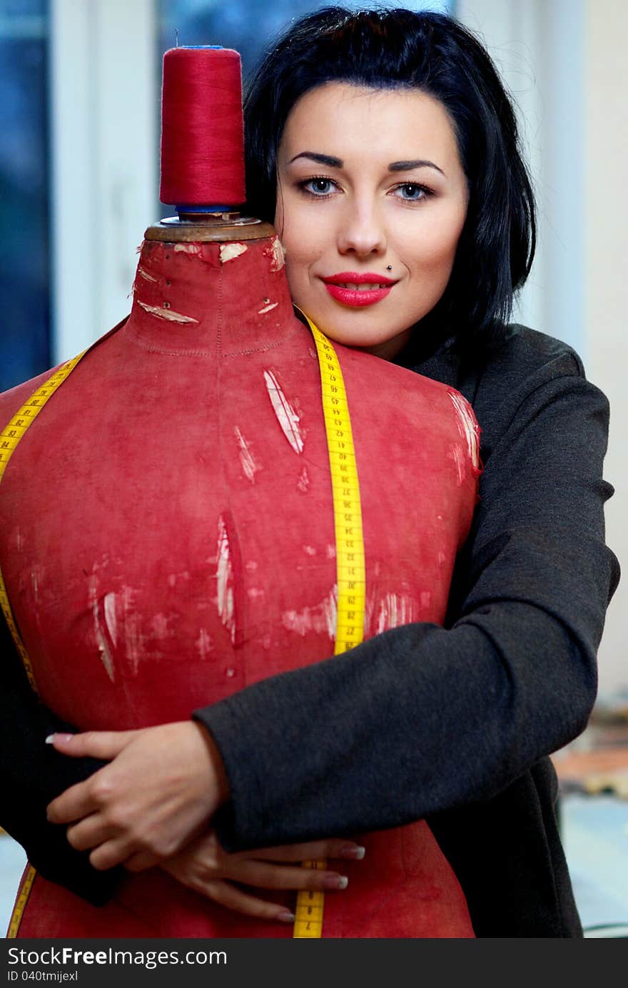 Seamstress with red old mannequin and measuring tape in her workshop