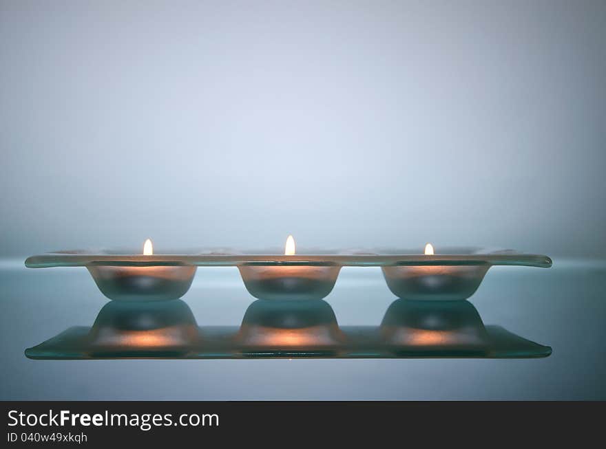 Three candles light in glass holder, on glass table