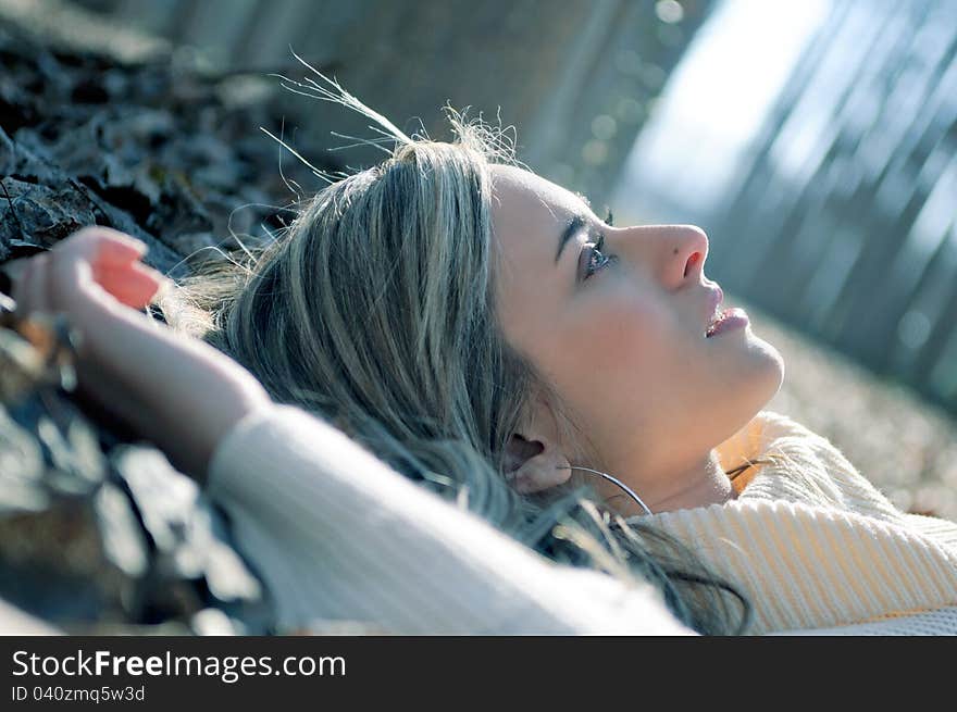 Beautiful blonde girl lying on leaves in a forest of poplars