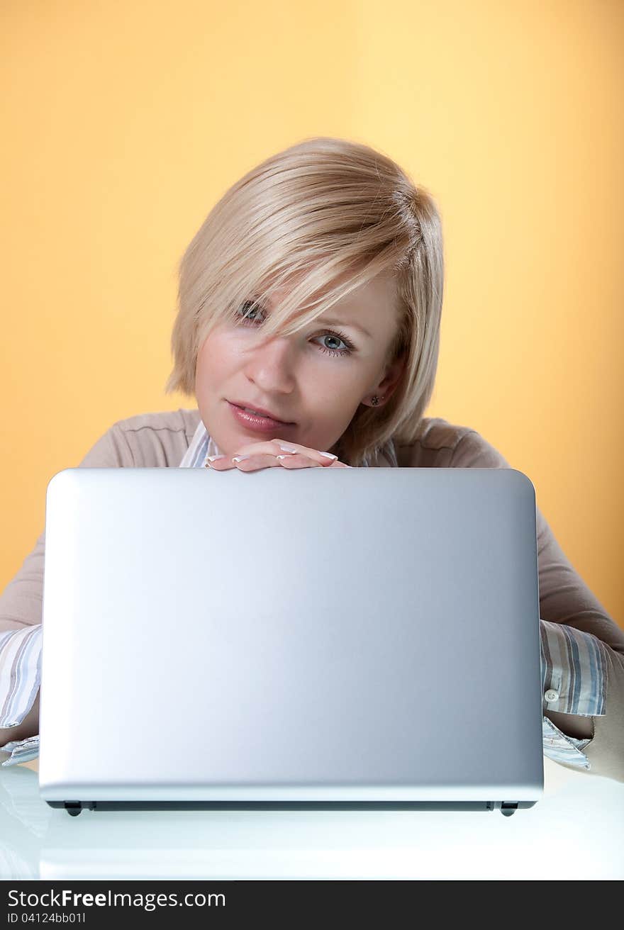 Young woman with a silver laptop on a yellow background looking in camera. Young woman with a silver laptop on a yellow background looking in camera