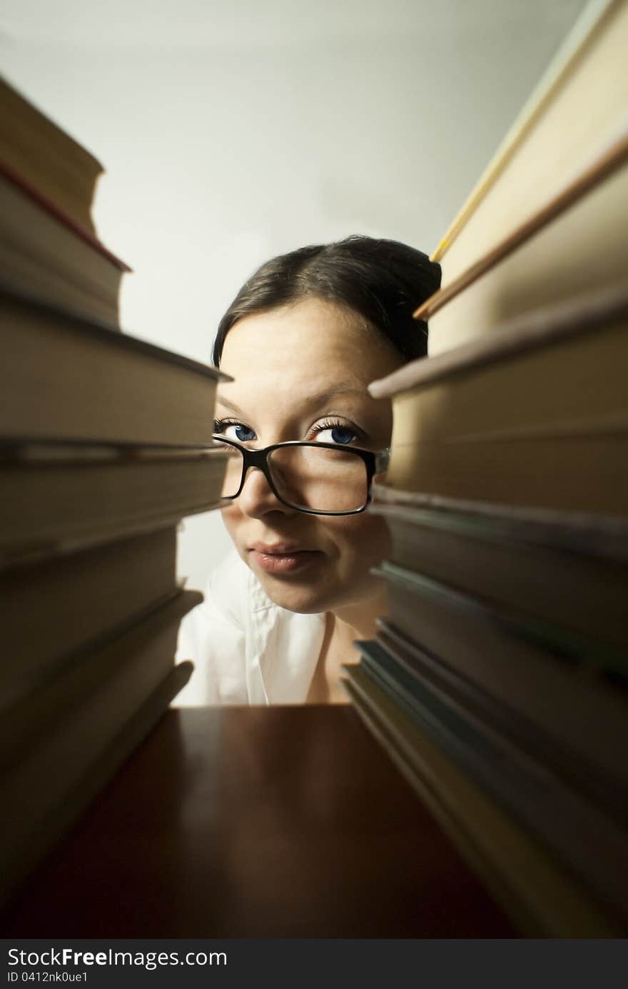 Brunette girl librarian, looks out over piles of books. Brunette girl librarian, looks out over piles of books