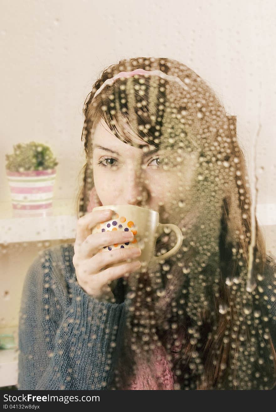 Young woman behind the glass drinking a tea. Young woman behind the glass drinking a tea