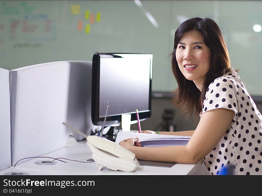 Asian girl at busy office smiling in front of computer. Asian girl at busy office smiling in front of computer.