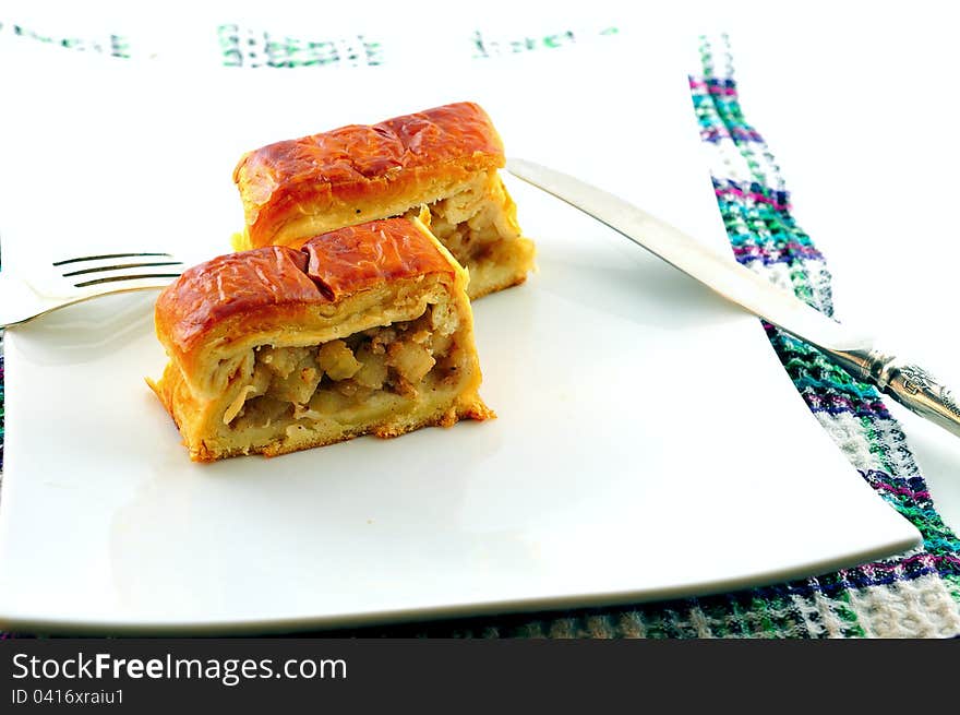 Two pieces of apple strudel are on a plate next to the fork and knife are