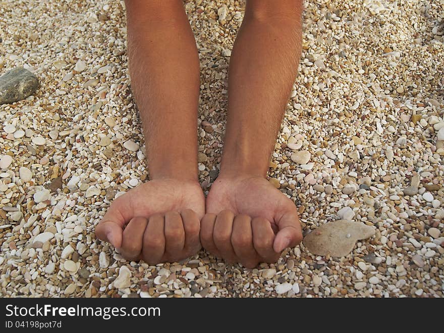 Man tanned hands compressed into cams against background of small stones on the beach. Man tanned hands compressed into cams against background of small stones on the beach