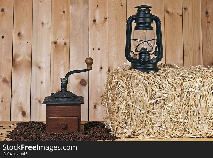 Coffee grinder and beans on wood background with lantern and straw bale