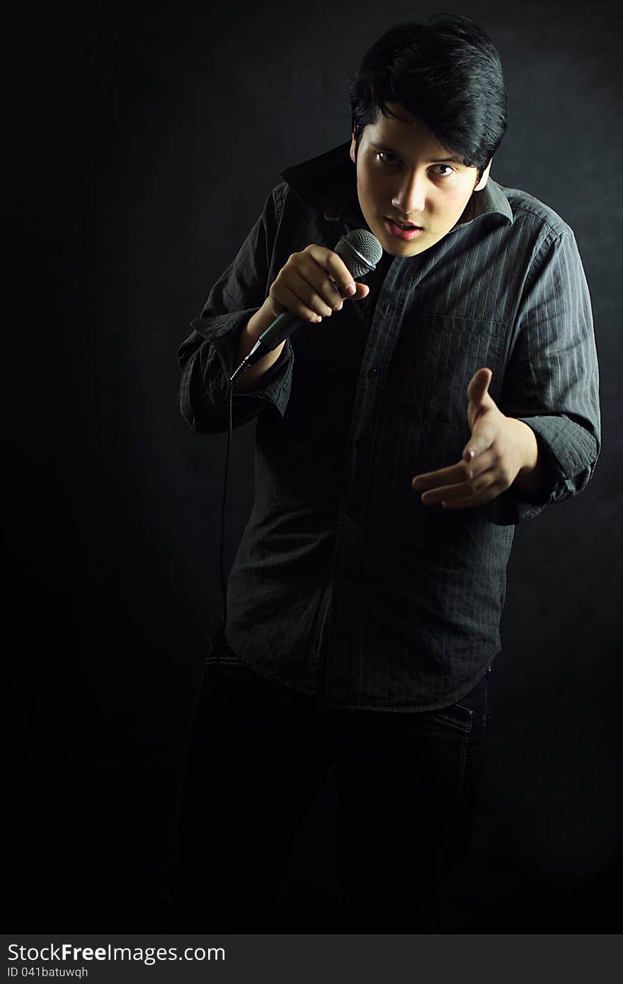 Young man singer with microphone gesture on black background