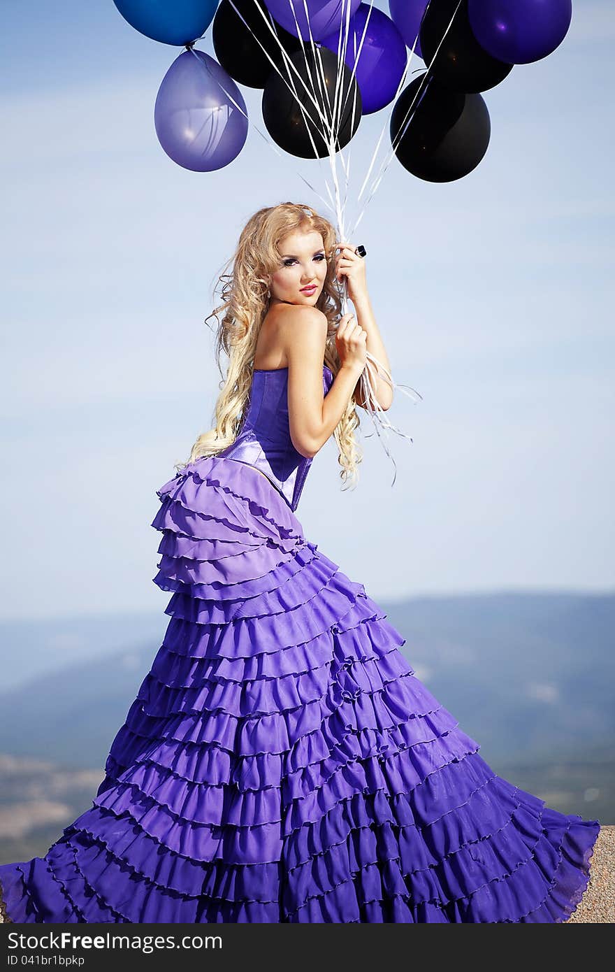 Beautiful girl in the purple dress with balloons in the background sky