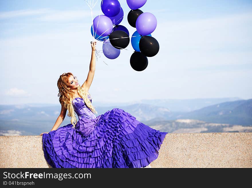 Beautiful girl in the purple dress with balloons in the background sky