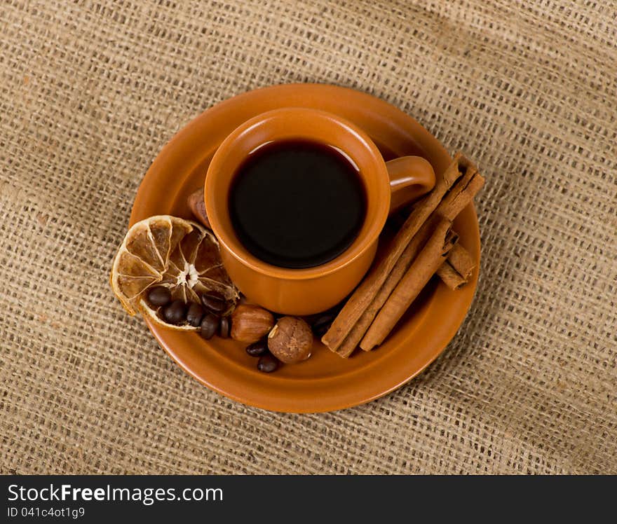 Closeup shot of freshly prepared cup of italian espresso with cinnamon, coffe beans, nuts and lemon over sacking. Closeup shot of freshly prepared cup of italian espresso with cinnamon, coffe beans, nuts and lemon over sacking