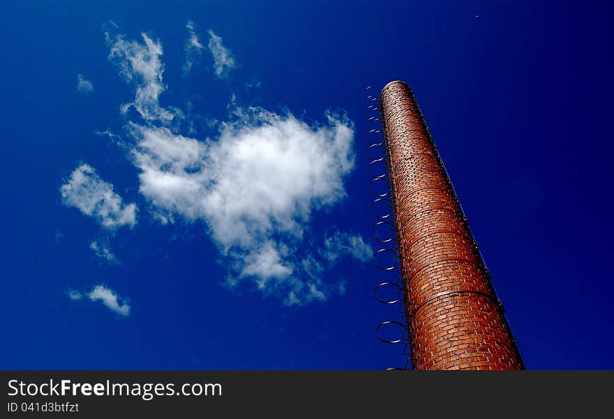 An old factory chimney, white clouds, blue sky.