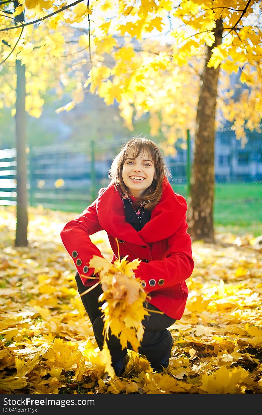 Young laughing woman in red coat is going to throw yellow leaves. Young laughing woman in red coat is going to throw yellow leaves