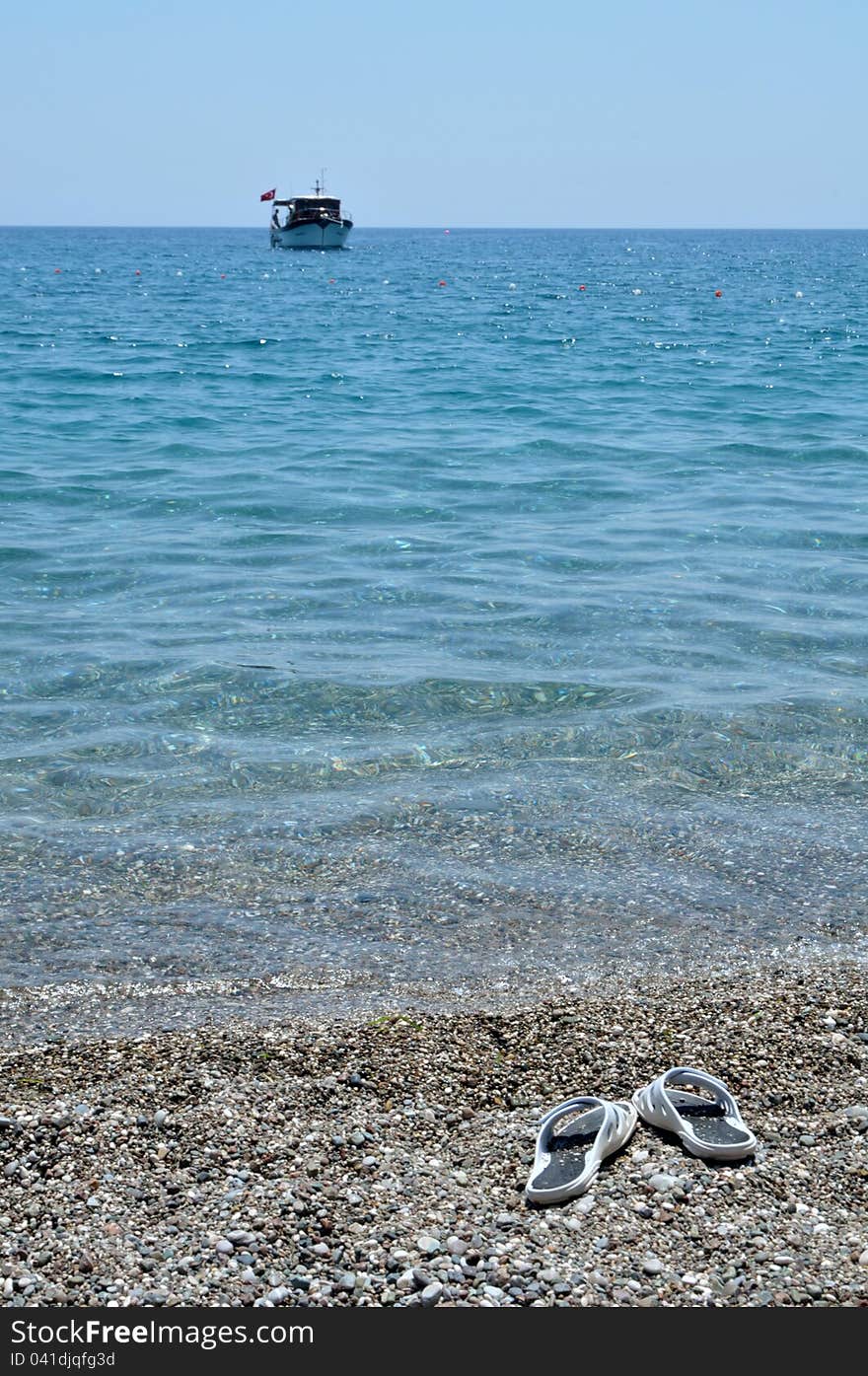 Slippers on the pebble beach and a boat in the sea