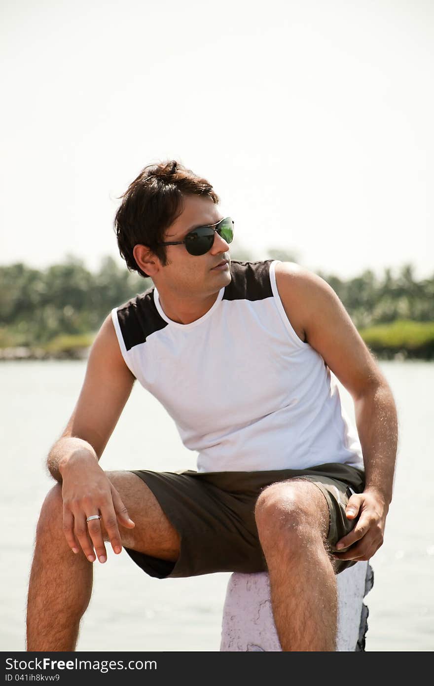 Indian Happy young man sitting on stone out of the water with sunglasses. Indian Happy young man sitting on stone out of the water with sunglasses