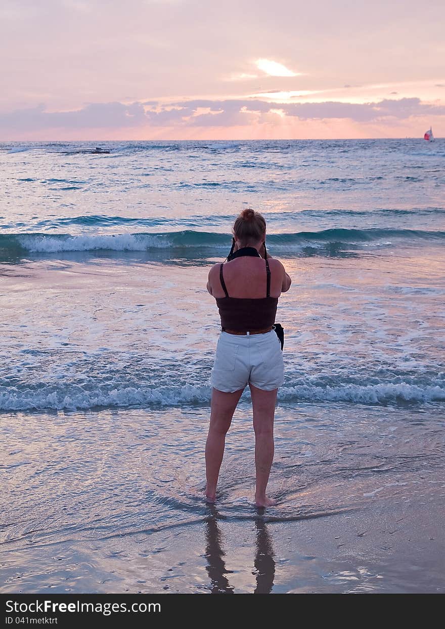 Attractive woman on a beach taking pictures with camera facing beautiful seascape sunset