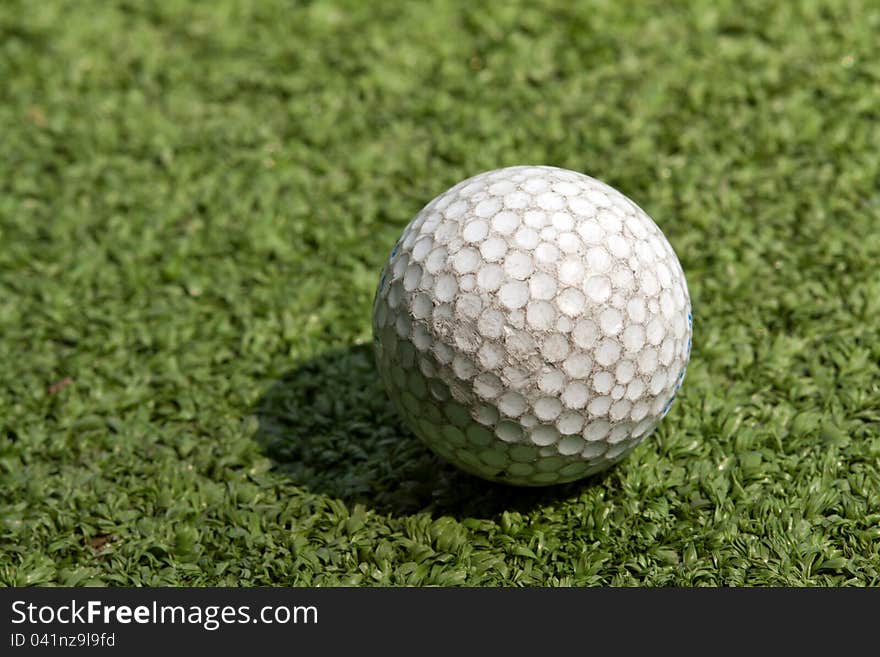 Old scratched dirty golf ball on artificial turf