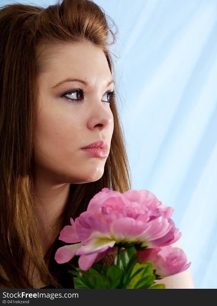 Beautiful brunette woman with romantic expression looking up slightly with pink and green flowers.  Textured sky blue background. Beautiful brunette woman with romantic expression looking up slightly with pink and green flowers.  Textured sky blue background