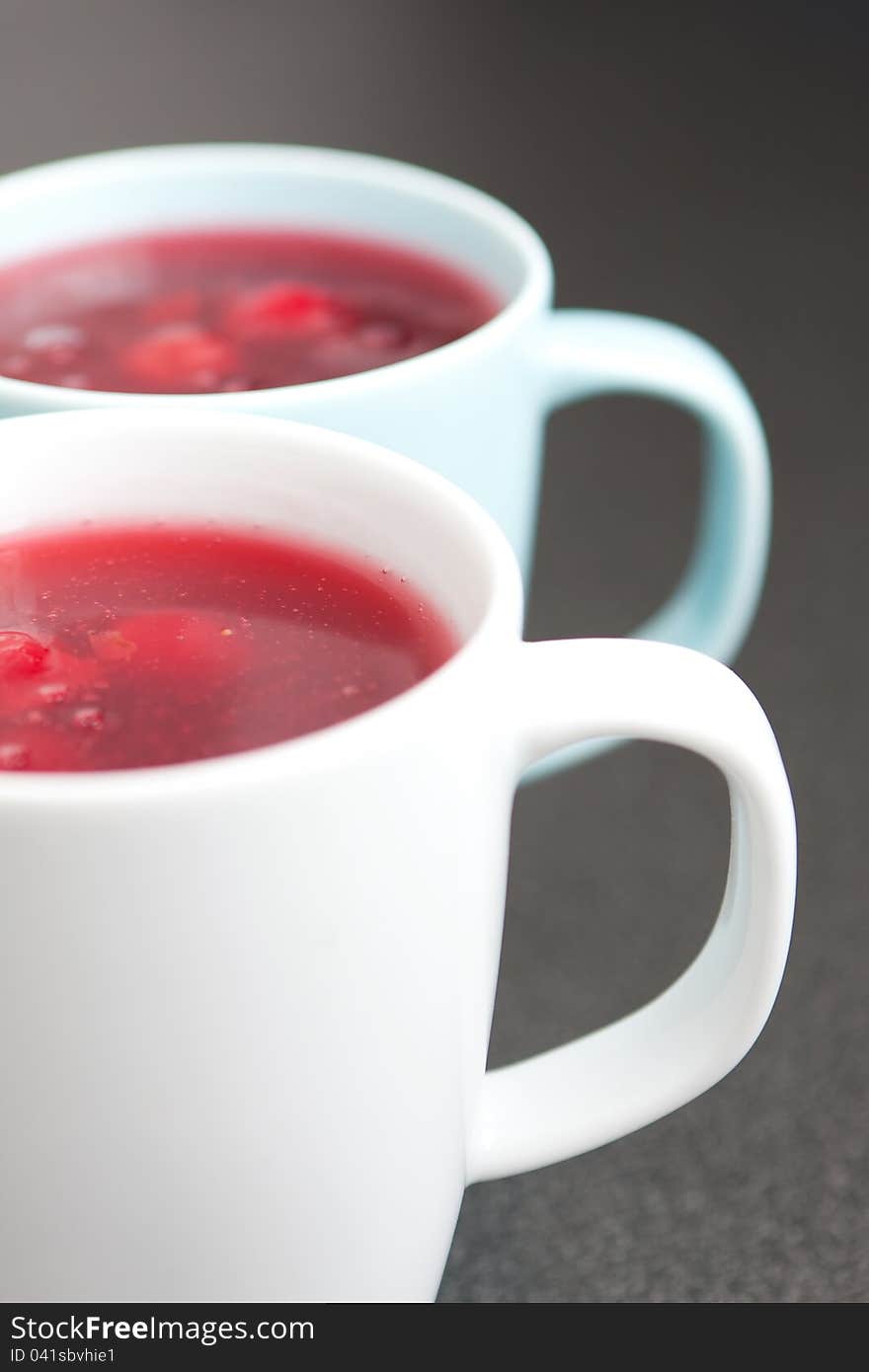 Two white ceramic mugs of fresh red fruit juice with fruit chunks, healthy eating