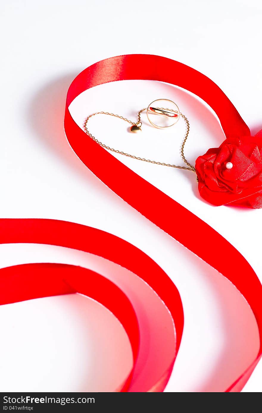 Golden wedding bands and chain with heart surrounded by red ribbon with rose bow on white background. Golden wedding bands and chain with heart surrounded by red ribbon with rose bow on white background