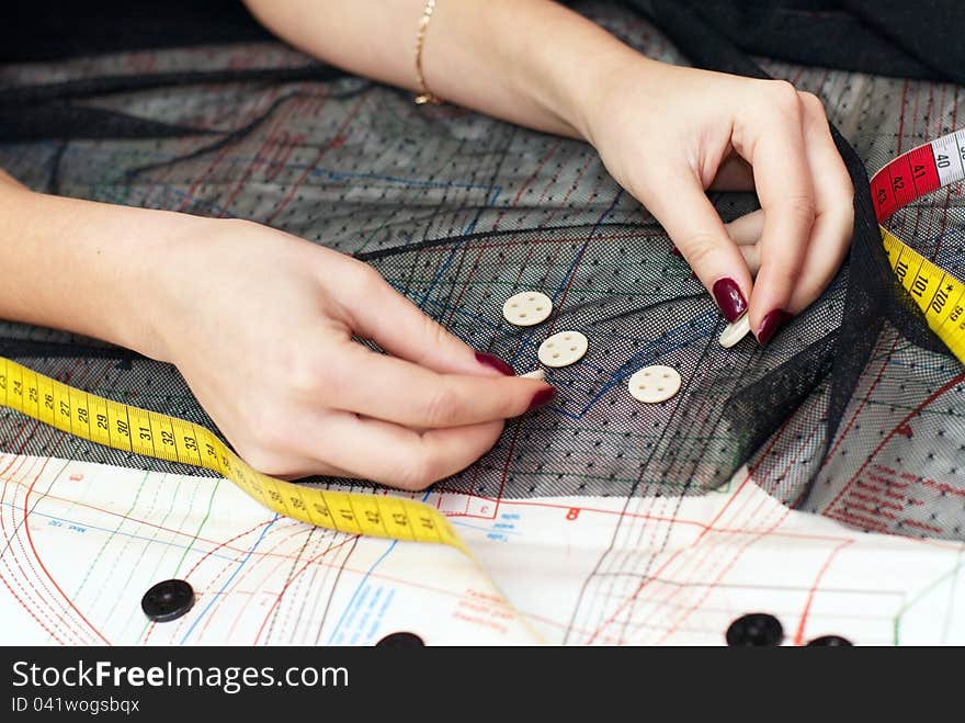 Female hands choosing buttons  on cloth over sewing pattern