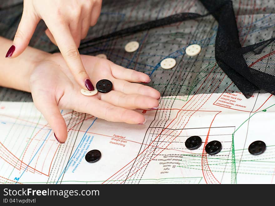 Female hands choosing buttons  on cloth over sewing pattern