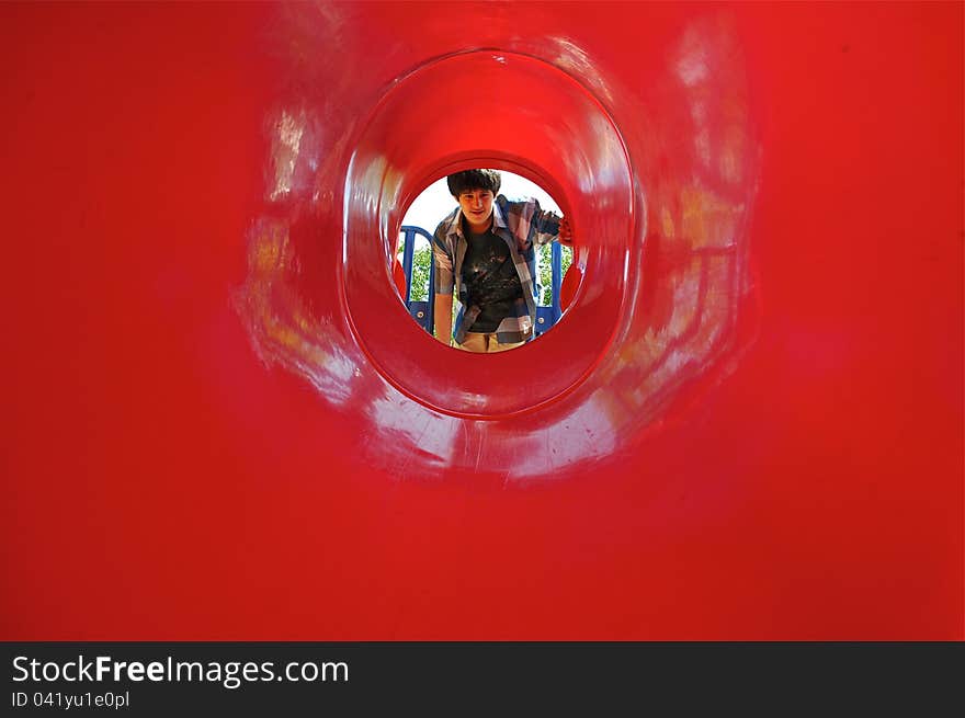 A boy is exploring a red tunnel in a playground.